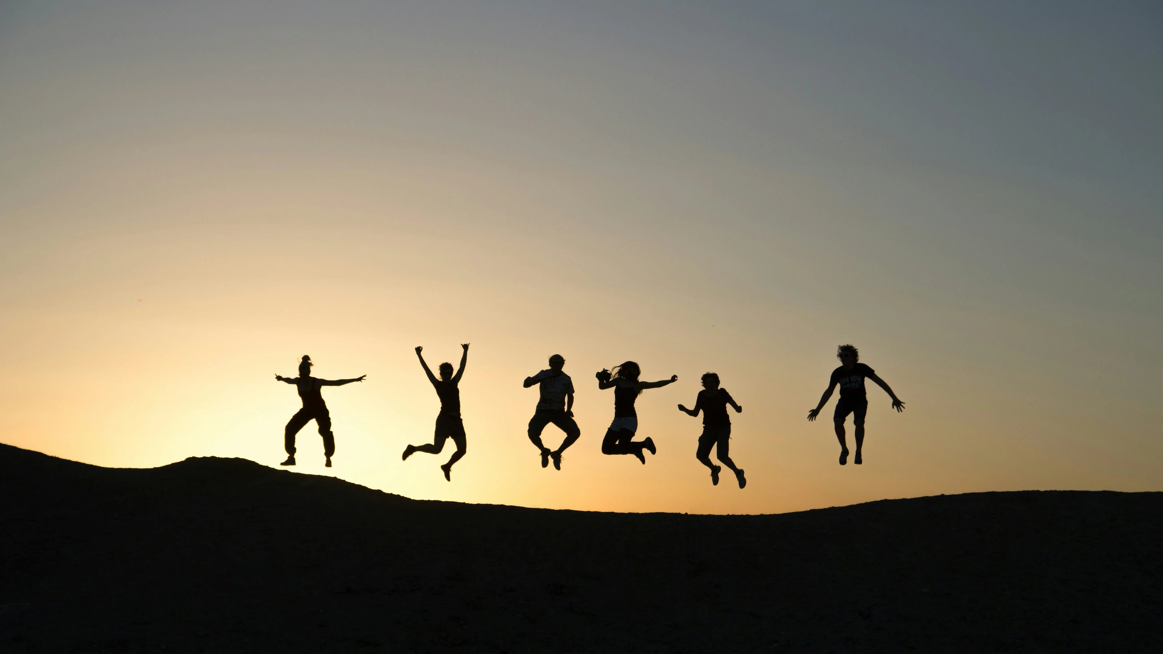 Silhouettes of people jumping against a sunset sky